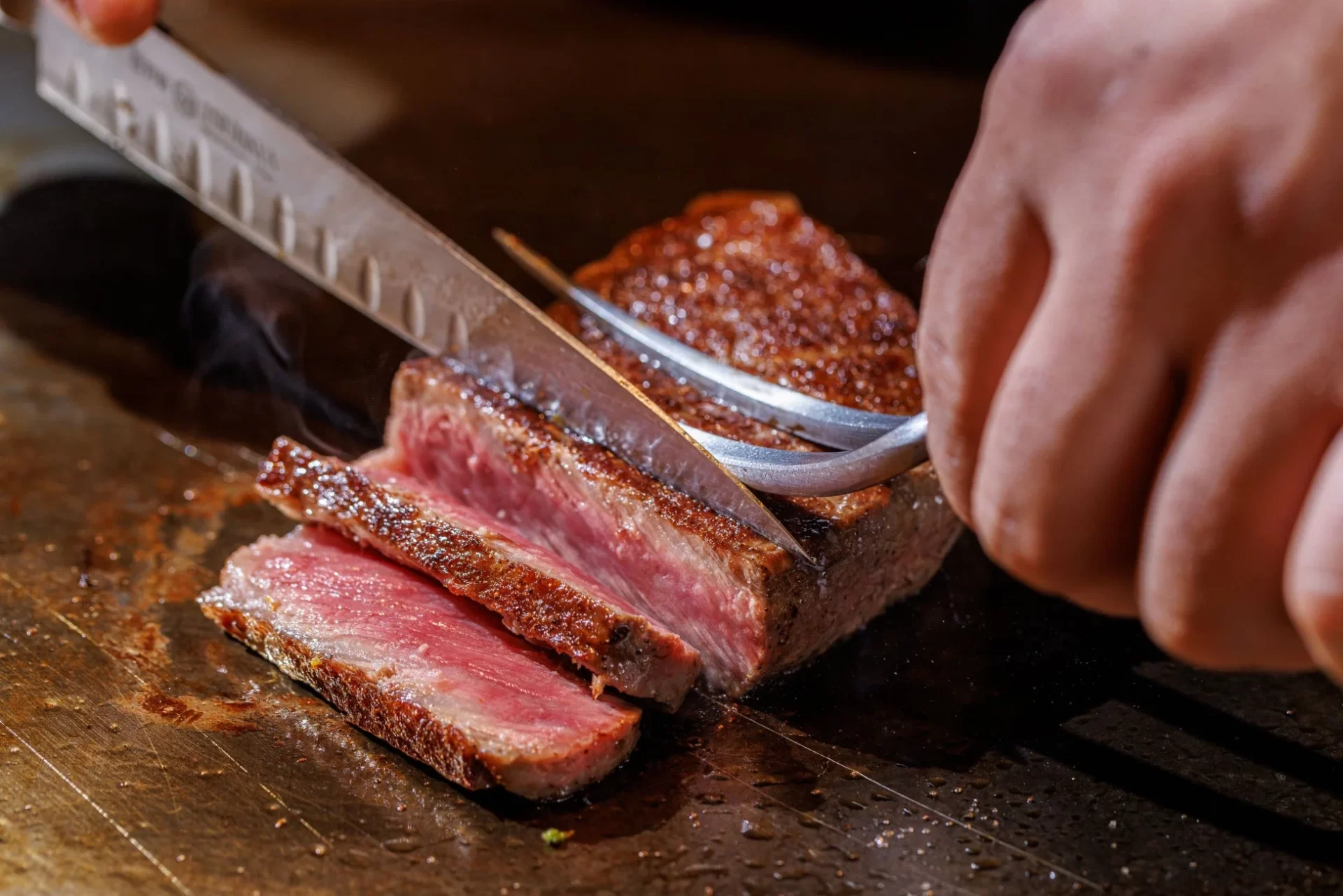 熱々のステーキが丁寧にスライスされている瞬間を捉えた画像です。ミディアムレアに焼かれた肉の断面が美しく、食欲をそそります。